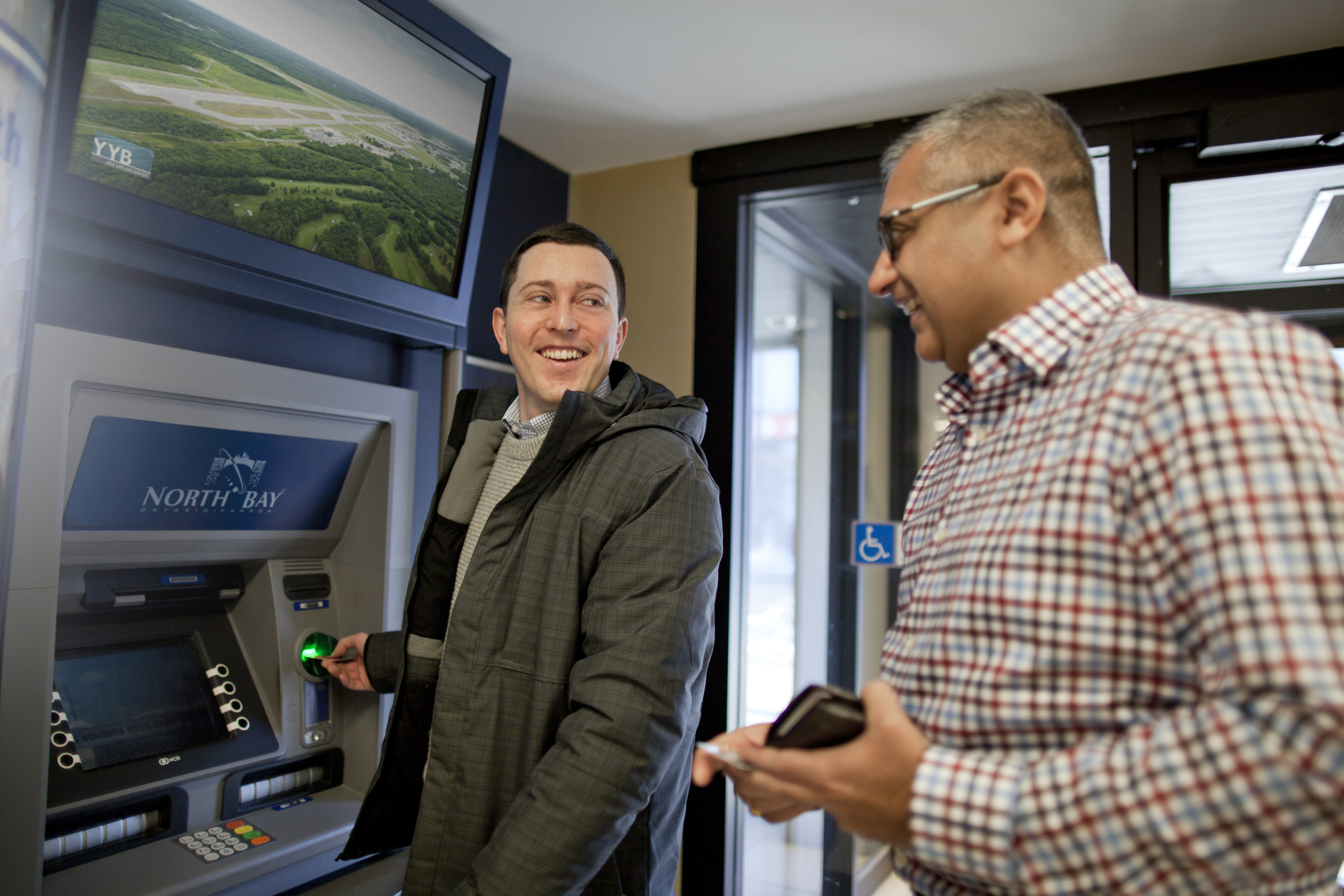 One person at an automatic banking machine, smiling at person standing behind them