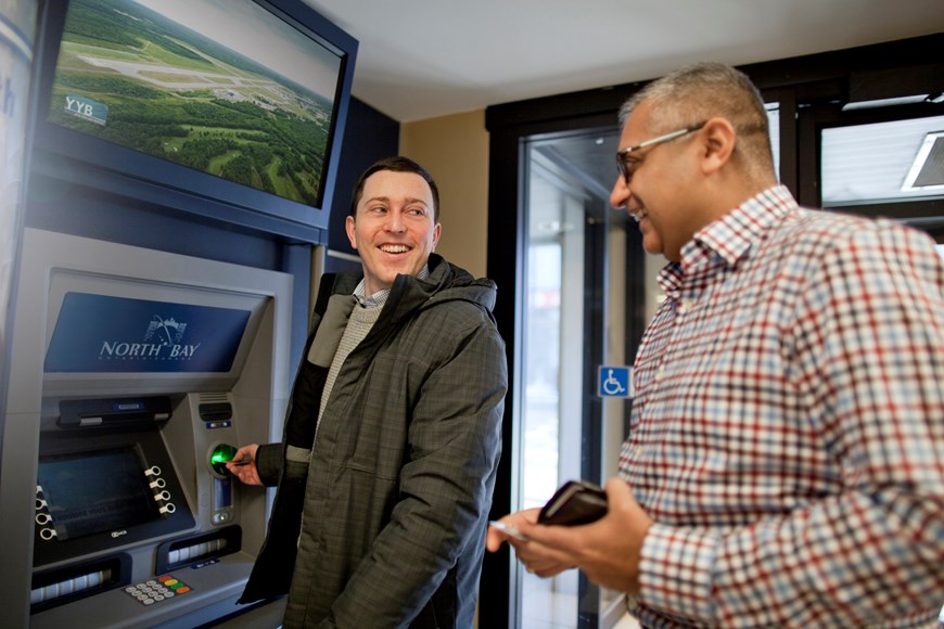 One person at an automatic banking machine, smiling at person standing behind them