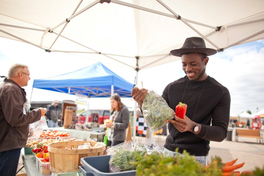 A man in a hat looks at produce at the local Farmers Market